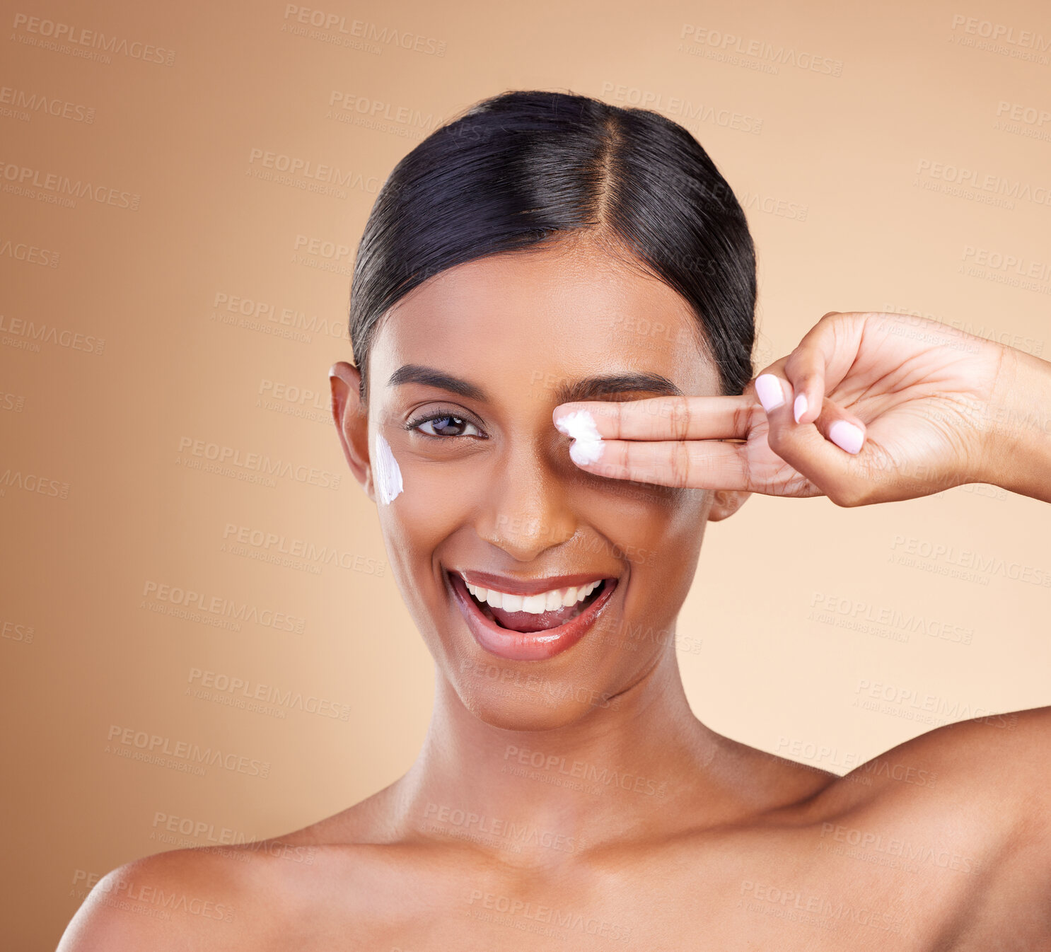 Buy stock photo Beauty, face cream and portrait of a woman in studio for skincare, dermatology and cosmetics. Happy Indian female model with smile and lotion on hand for self care moisture facial on brown background