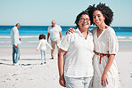 Portrait, summer with a mother and daughter on the beach during summer while their family play in the background. Love, smile or nature with a senior woman and adult child bonding outdoor together