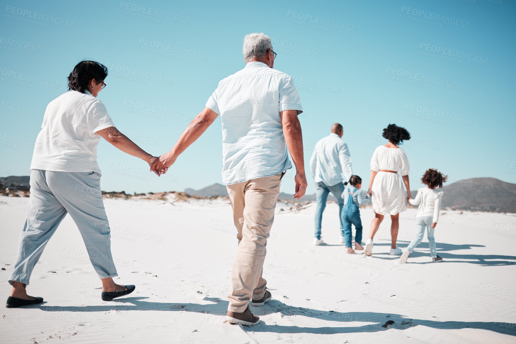 Buy stock photo Elderly couple, holding hands and family at beach with back for walk, freedom and vacation together with love. Old man, woman and grandchildren by ocean for walking, wellness and journey in sunshine