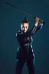 Woman, warrior and vigilante in cosplay with sword ready for battle, war or game against a dark studio background. Female in black widow costume with guns and blade for halloween or hunger games