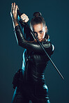 Woman, warrior and vigilante in cosplay with sword for dangerous battle, war or game against dark studio background. Portrait of female in black widow costume with blade for halloween or hunger games