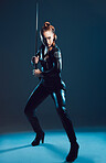 Woman, warrior and vigilante in cosplay with sword stance for battle, war or game against dark studio background. Female in black widow costume standing ready with blade for halloween or hunger games