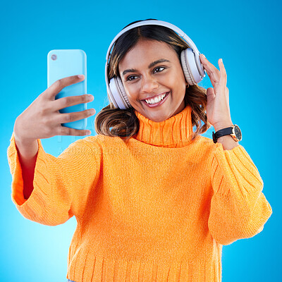 Buy stock photo Music headphones, smile and selfie of woman in studio isolated on a blue background. Profile picture, radio and happy Indian female streaming, listening and enjoying sound, audio podcast or song.