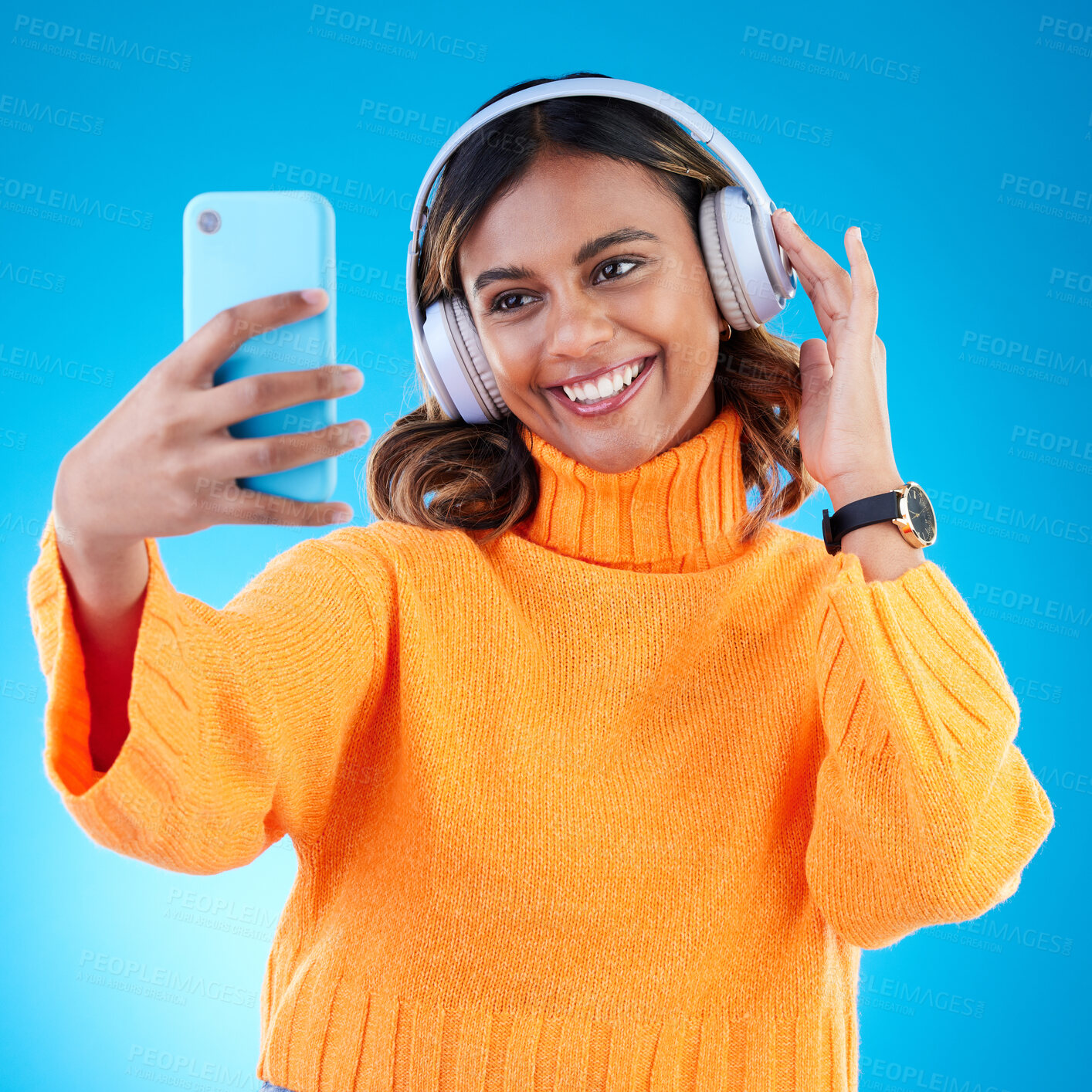 Buy stock photo Music headphones, smile and selfie of woman in studio isolated on a blue background. Profile picture, radio and happy Indian female streaming, listening and enjoying sound, audio podcast or song.