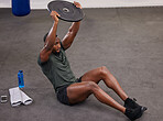 Black man holding weight plate for fitness, exercise and workout in gym. Strong bodybuilder weightlifting on floor for power, energy and heavy sports challenge in training, muscle gain and balance 