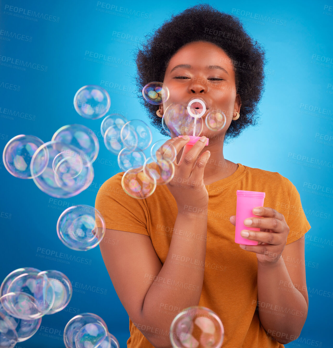 Buy stock photo Fun, bubbles and black woman with joy, positive attitude and happiness against a blue studio background. African American female, lady and soap bubble for joy, playing and cheerful with excitement