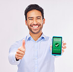 Asian man, portrait and phone with thumbs up for transaction approval against a white studio background. Happy male smile showing thumb emoji, yes sign or like for electronic purchase on smartphone
