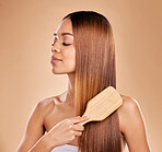 Brushing hair, beauty and woman with growth and shine for healthy texture on a brown background. Smile of aesthetic female happy in studio with a brush for natural keratin treatment haircare results