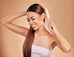 Smile, beauty and woman brushing hair for growth and shine for healthy texture on brown background. Aesthetic female model happy in studio with a brush for natural keratin treatment haircare results