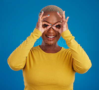 Buy stock photo Black woman, binocular hands and eyes in studio portrait for comic funny face with smile, fashion and happy. Student girl, model and ok hand gesture with happiness, youth and pride by blue background