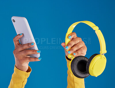 Buy stock photo Closeup, hands and smartphone with headphones, streaming music and audio against blue studio background. Zoom, hand and technology with cellphone, headset or radio with sounds, internet or connection