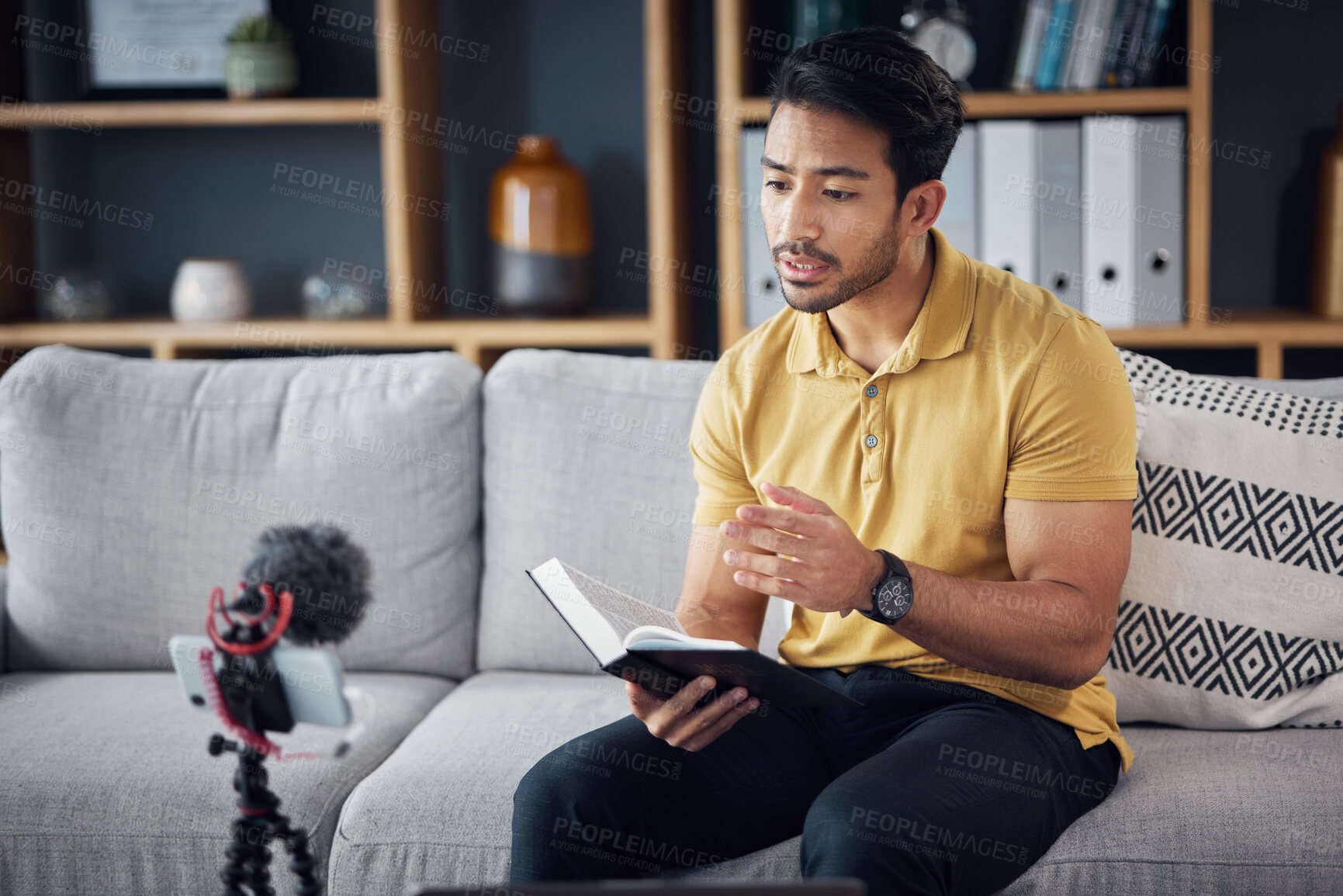 Buy stock photo Podcast, bible study and phone with a man online to preach or reading while live streaming. Asian male on home sofa with Christian scripture or book as content creator teaching on education religion