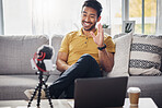 Laptop, phone and content creation, Indian man on sofa, webinar recording and live streaming in home. Internet, webcam and online influencer with smile, wave and equipment for social media channel.