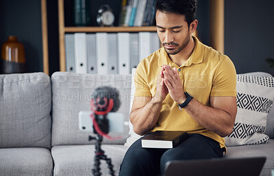 Buy stock photo Podcast, bible and man pray with a phone and microphone online while live streaming. Asian male on home sofa to pray with hands and Christian religion book as blog content creator or influencer 