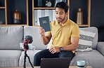 Podcast, bible and man talking on phone and microphone online while live streaming. Asian male on home sofa with Christian religion book as blog content creator or influencer teaching or studying