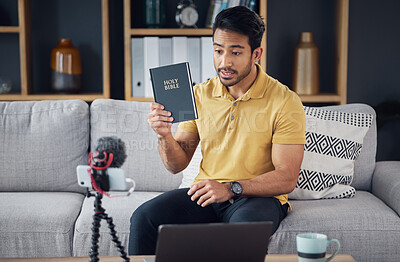 Buy stock photo Streaming, bible and man talking on phone and microphone online for live podcast. Asian male on home sofa with Christian religion book as blog content creator or influencer teaching or studying