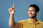 Finger, pointing and happy man in studio with hand gesture, sign or showing mockup on blue background. Smile, point and asian male with idea on space for advertising, product placement and isolated