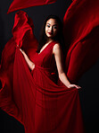 Portrait of woman, art and fashion, fabric on dark background with beauty and aesthetic movement. Flowing silk motion, fantasy and artistic model with smile in red creative designer dress in studio.
