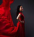 Happy woman, art and fashion, red fabric on dark background with beauty and aesthetic movement. Flowing silk, fantasy and artistic model with smile in creative designer dress in studio with motion.