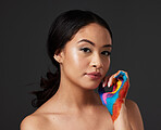 Woman, portrait and beauty with rainbow paint hand and skincare for serious face in studio. Creative skin and makeup on female aesthetic model on gray background for lgbtq color inspiration on hands