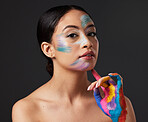 Woman, beauty and portrait with rainbow hand paint art on face in studio with glow. Creative skin and makeup on female aesthetic model serious on gray background for lgbtq color inspiration on hands