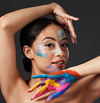 Woman, portrait and beauty with rainbow paint art on hand and face in studio with a smile. Creative skin and makeup on female aesthetic model on gray background for lgbtq color inspiration on hands