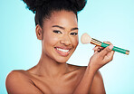 Black woman, brush and makeup in studio with smile for wellness, cosmetics or youth by blue background. Model, girl and african with foundation, powder and happy for skincare, beauty and healthy glow