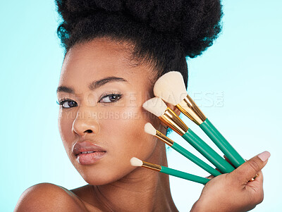 Buy stock photo Portrait, brushes and black woman with makeup, foundation and glow against a blue studio background. Face, Nigerian female and lady with cosmetic tools, grooming and morning routine for smooth skin 