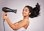 Portrait, blow dry and hair with a woman in studio on a gray background holding an appliance. Salon, smile and hairdryer with an attractive young female model drying her hairstyle for beauty