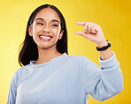 Hand gesture, pinch and measure with a woman on a yellow background in studio to show a size. Smile, review and icon or symbol with an attractive young female posing on a color wall for growth