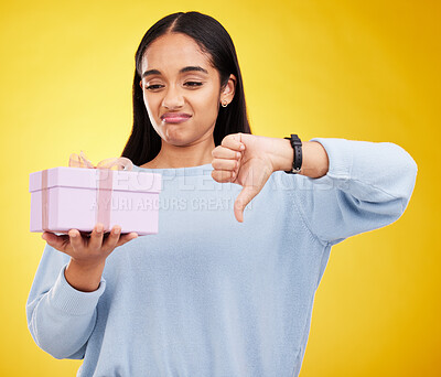 Buy stock photo Gift, box and woman with thumbs down on yellow background for negative, disagreement and bad sign. Emoji mockup, sadness and girl holding present with dislike, unhappy and disappointed hand gesture