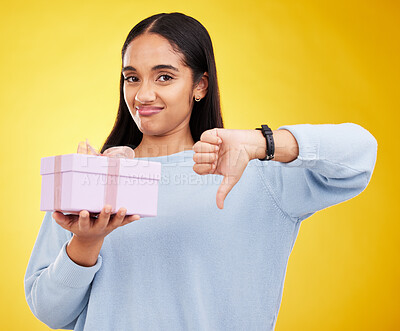 Buy stock photo Disappointed, portrait and woman with a thumbs down for a gift isolated on a yellow background. Unhappy, negative and a girl holding a present and showing a hand gesture for disappointment in studio