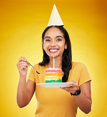Buy stock photo Woman is eating birthday cake, celebration and happy in portrait, rainbow dessert and candle on yellow background. Celebrate, festive and young female, excited for sweet treat and party hat in studio