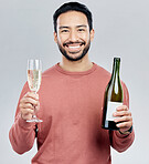 Portrait, champagne and cheers with a man in studio on a gray background holding a bottle for celebration. Glass, alcohol and toast with a handsome young man celebrating the new year tradition