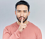 Secret, finger on lips and portrait of man in studio with privacy, silence and confidential hand gesture. Communication mockup, emoji and face of male on grey background for shush, whisper or gossip