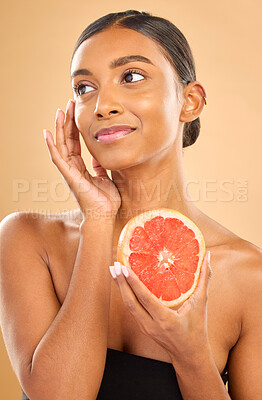 Buy stock photo Skincare, beauty and woman with a grapefruit for a glow isolated on a studio background. Thinking, smile and an Indian model with a fruit for healthy skin, complexion and vitamin c treatment