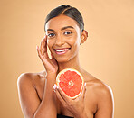Skincare, portrait and a woman with a grapefruit for a glow isolated on a studio background. Food, smile and an Indian model with a fruit for healthy skin, complexion and vitamin c treatment