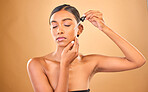 Face, skincare serum and woman with eyes closed in studio isolated on brown background. Dermatology, cosmetics and Indian female model apply hyaluronic acid, retinol or essential oil for healthy skin