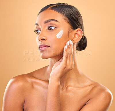 Buy stock photo Face, beauty skincare and woman with cream in studio isolated on a brown background. Dermatology, cosmetics idea and thinking Indian female model with lotion, creme or moisturizer for skin health.