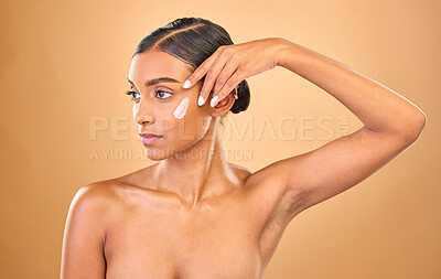 Buy stock photo Face, skincare beauty and woman with cream in studio isolated on a brown background. Dermatology idea, cosmetics and thinking Indian female model with lotion, creme or moisturizer for skin health.