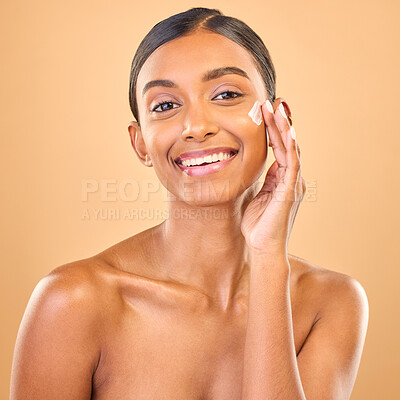 Buy stock photo Face portrait, skincare and woman with cream in studio isolated on a brown background. Dermatology smile, cosmetics and happy Indian female model apply lotion, creme and moisturizer for healthy skin.