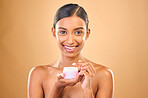 Face, skincare and woman with cream jar in studio isolated on a brown background. Dermatology cosmetics, portrait and happy Indian female apply lotion, creme and moisturizer product for healthy skin.