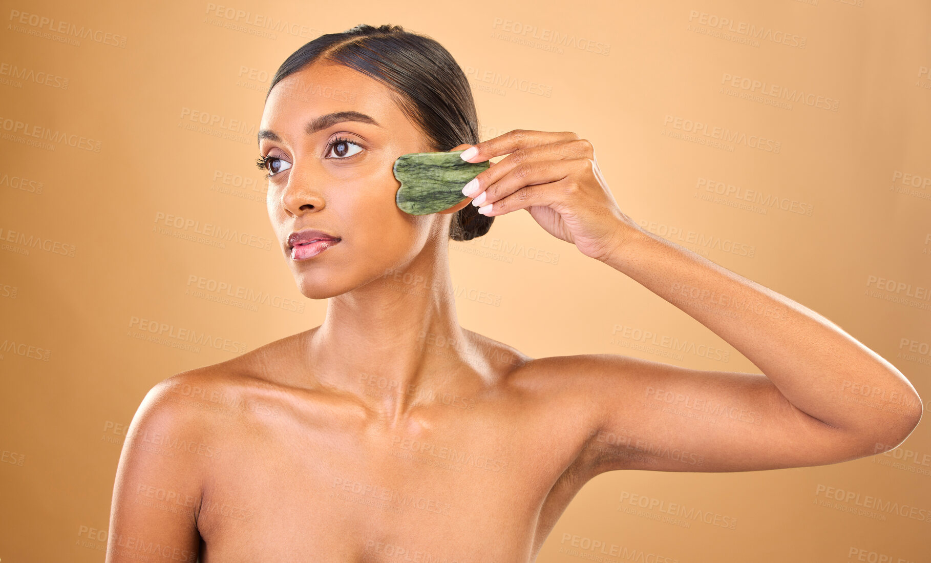 Buy stock photo Face, beauty skincare and woman with gua sha in studio isolated on a brown background. Dermatology, thinking and serious Indian female model with jade crystal or stone for healthy skin treatment.