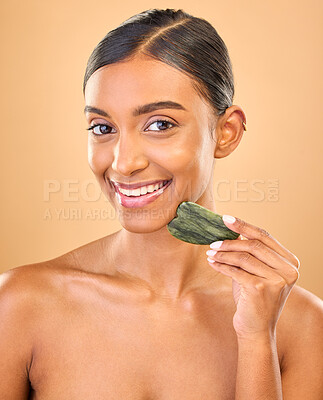Buy stock photo Face smile, skincare and woman with gua sha in studio isolated on a brown background. Dermatology portrait, massage and happy Indian female model with jade crystal or stone for healthy skin treatment
