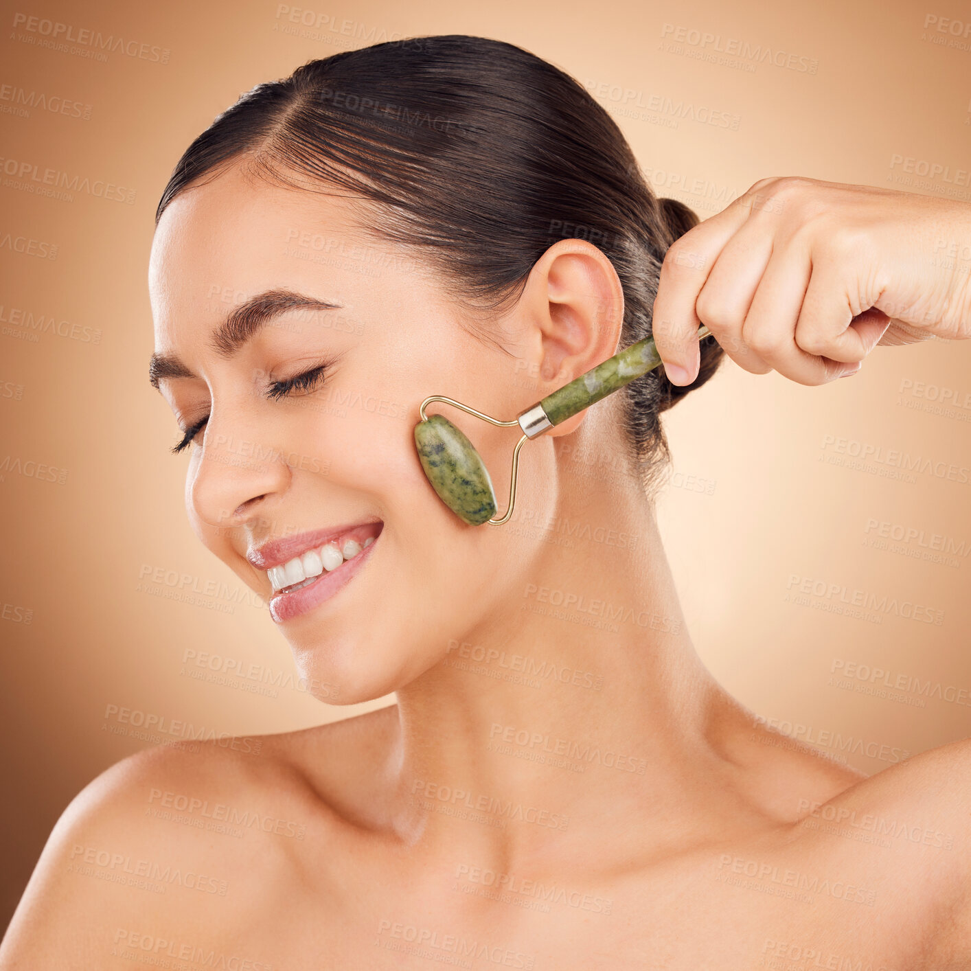 Buy stock photo Skincare, jade roller and happy woman in studio for beauty, wellness and anti aging against brown background. Facial, skin and girl relax with massaging tool, facelift and lymphatic drainage isolated