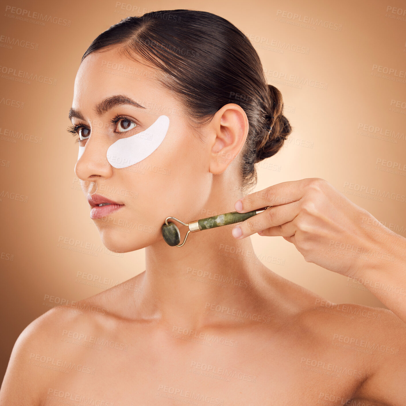 Buy stock photo Woman beauty, eye patch and face roller for studio dermatology, healthcare or skincare treatment. Facial massage product, dermatology or female model with hyaluronic acid mask on brown background