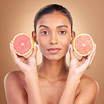 Indian woman, grapefruit and studio portrait for beauty, health or wellness with fruit by brown background. Asian young model and girl with organic citrus fruits for health, cosmetic and skin glow