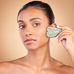 Beauty, gua sha and portrait of Indian woman for skincare, facial treatment and wellness with spa tools. Salon, dermatology and girl on brown background with cosmetics, face massage and luxury stone