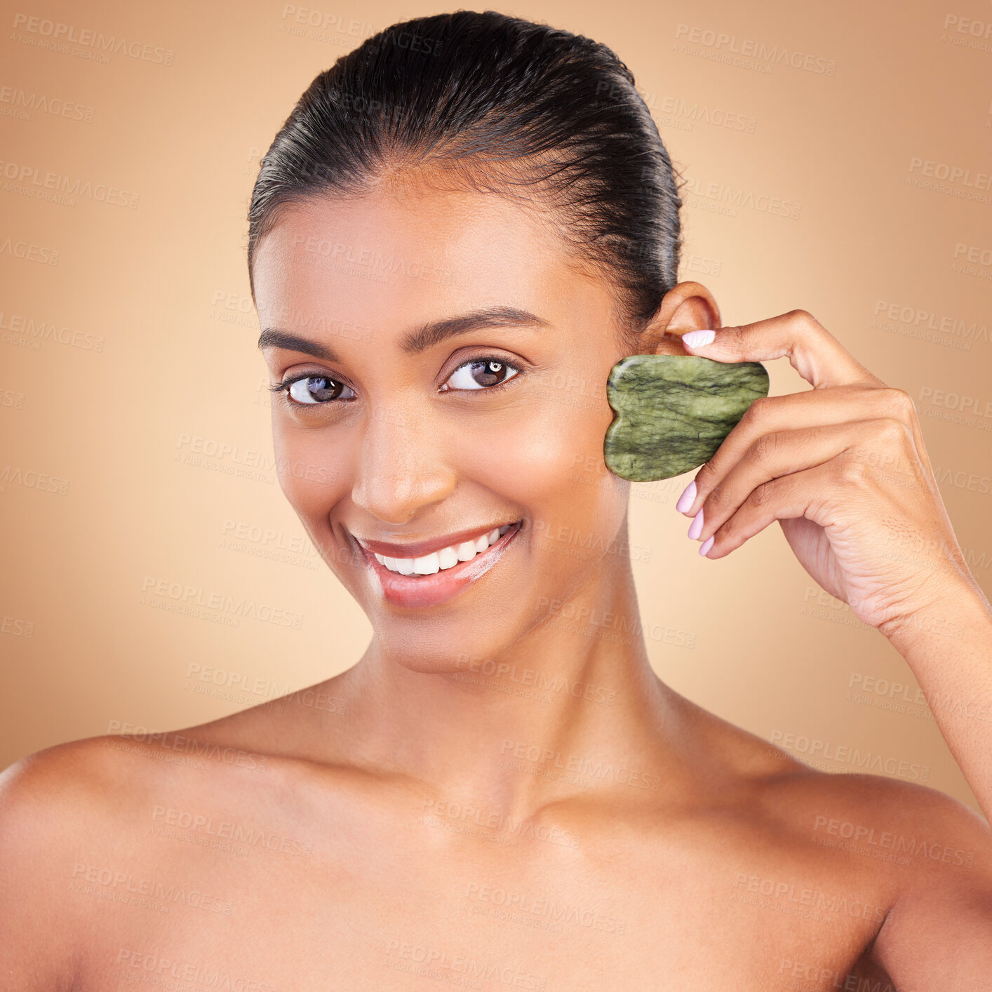 Buy stock photo Beauty, gua sha and portrait of Indian woman with smile for skincare, facial treatment and spa wellness. Salon, dermatology and girl on brown background with cosmetics, face massage and luxury stone