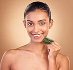 Beauty, gua sha and portrait of Indian woman with smile for skincare, facial treatment and spa wellness. Salon, dermatology and happy girl on brown background with cosmetics, face massage and stone